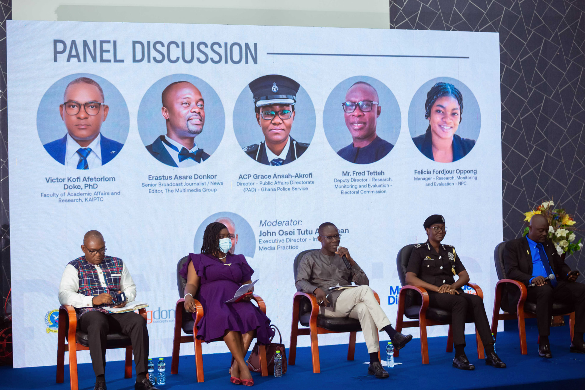 The panel discussion, with the panellists' profiles displayed on the screen behind them