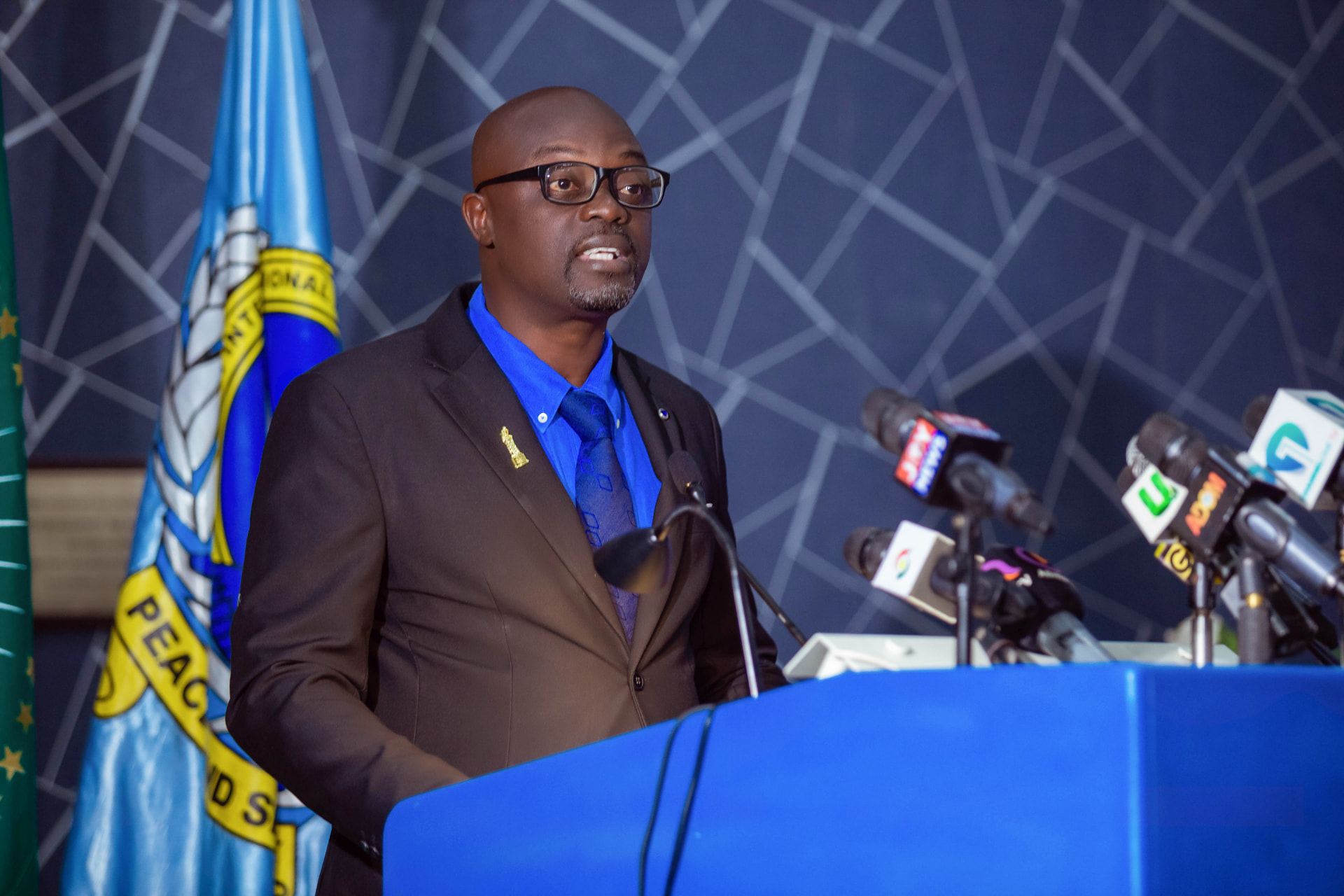 A speaker at the podium, with the KAIPTC flag behind him